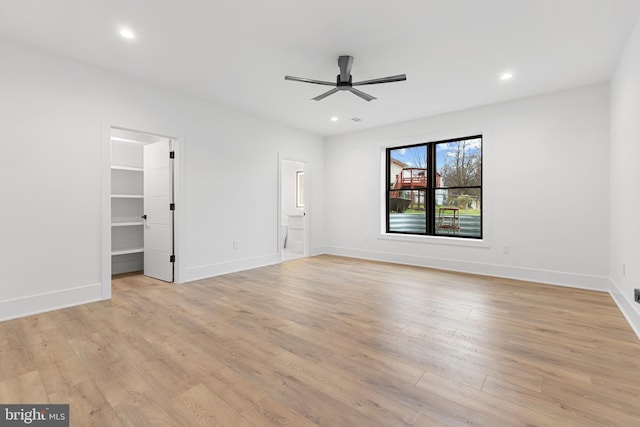 interior space with ensuite bath, a walk in closet, ceiling fan, and light wood-type flooring