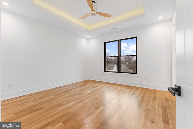 unfurnished room featuring ceiling fan, a tray ceiling, and light wood-type flooring