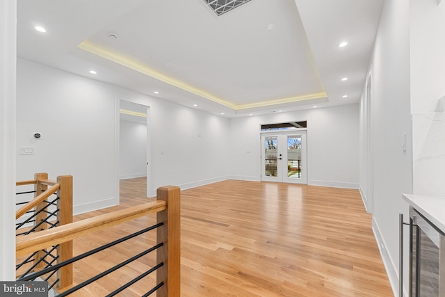 living room with wine cooler, a tray ceiling, light hardwood / wood-style flooring, and french doors