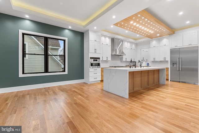 kitchen featuring appliances with stainless steel finishes, a large island, wall chimney range hood, and a tray ceiling