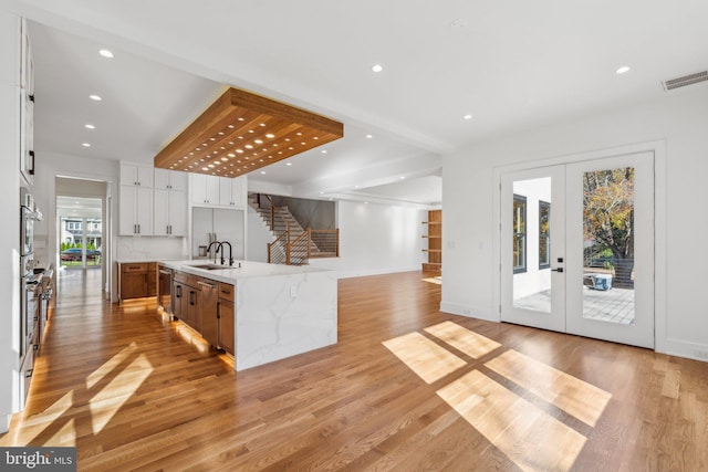 kitchen with white cabinetry, sink, a large island, light stone counters, and french doors