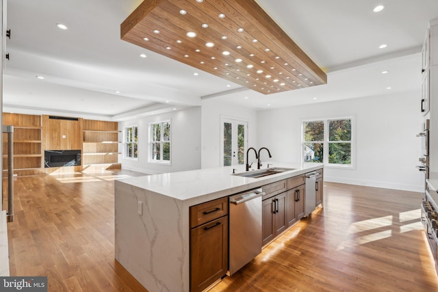 kitchen with a spacious island, sink, light stone counters, light wood-type flooring, and stainless steel appliances