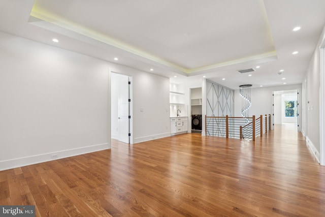 interior space with a raised ceiling, washer / dryer, hardwood / wood-style floors, and built in features