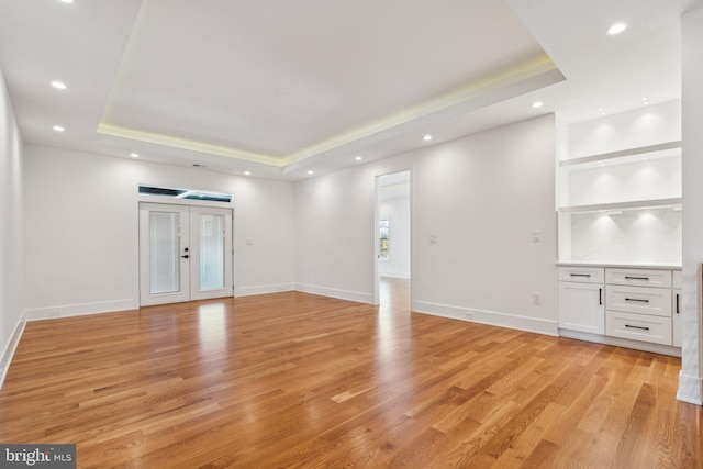 unfurnished living room featuring french doors, a raised ceiling, light hardwood / wood-style floors, and built in shelves