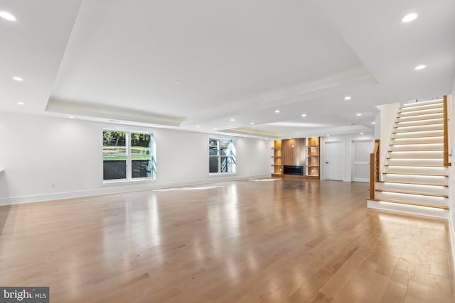 unfurnished living room featuring a tray ceiling and light hardwood / wood-style flooring