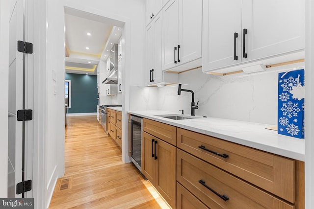 kitchen featuring wine cooler, sink, white cabinetry, light stone counters, and light hardwood / wood-style flooring