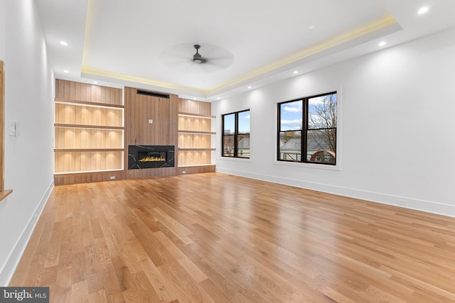 unfurnished living room featuring a fireplace, a tray ceiling, light hardwood / wood-style flooring, and built in features