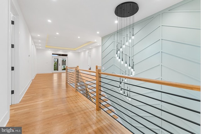 corridor featuring french doors, a tray ceiling, and light hardwood / wood-style flooring