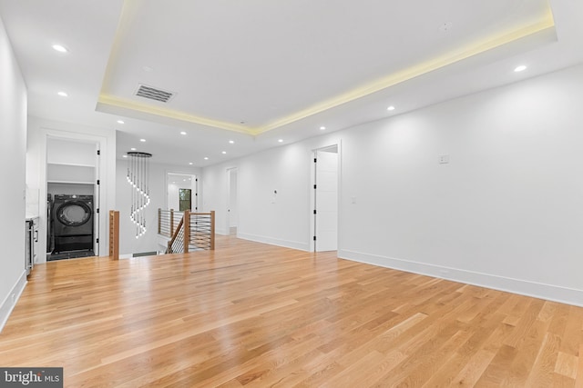 unfurnished living room featuring stacked washer / dryer, a tray ceiling, and light hardwood / wood-style flooring