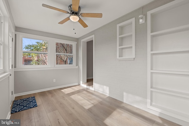 spare room with built in shelves, brick wall, ceiling fan, and light wood-type flooring