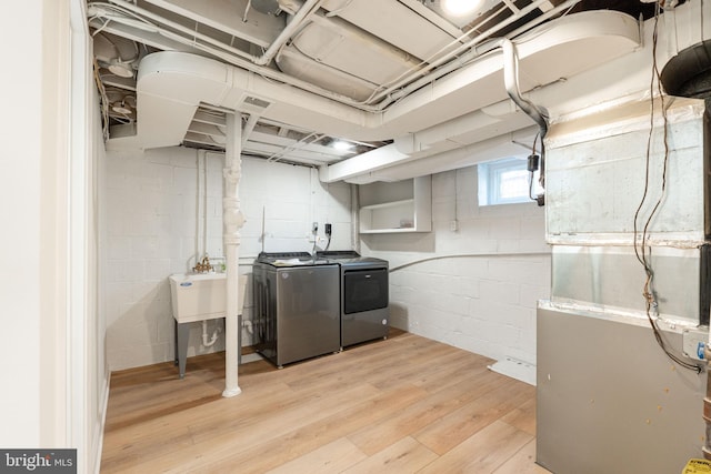 basement with washing machine and clothes dryer, sink, heating unit, and light wood-type flooring