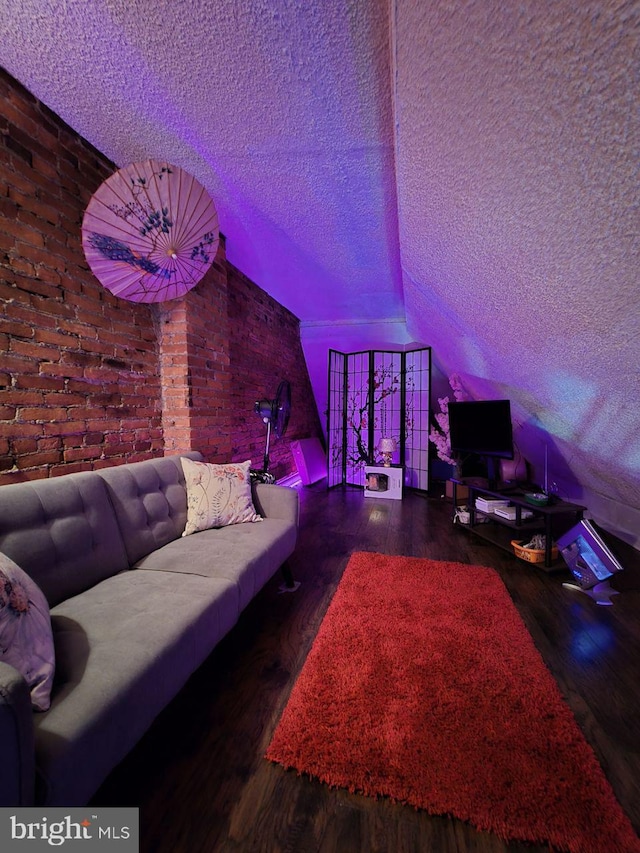 living room with brick wall, dark hardwood / wood-style floors, and a textured ceiling