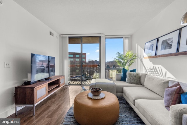 living room featuring a wall of windows, visible vents, baseboards, and wood finished floors