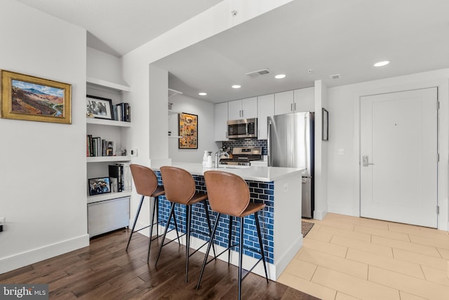 kitchen with light countertops, visible vents, appliances with stainless steel finishes, white cabinetry, and a kitchen breakfast bar