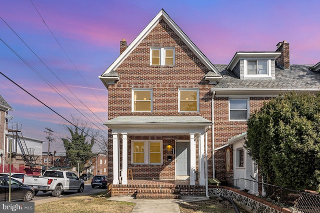 traditional home with covered porch, fence, and brick siding