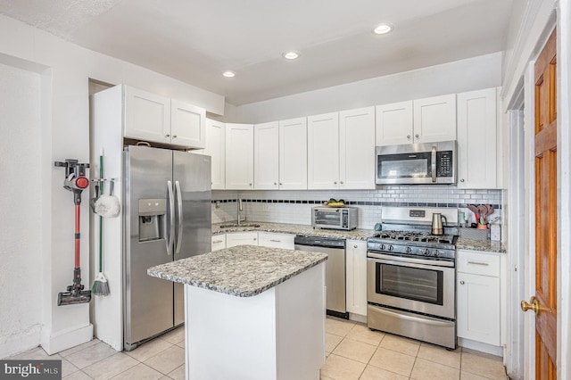 kitchen featuring tasteful backsplash, appliances with stainless steel finishes, white cabinets, light tile patterned flooring, and a kitchen island
