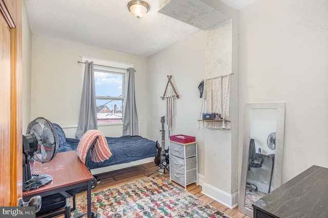 bedroom featuring a textured wall, a textured ceiling, baseboards, and wood finished floors
