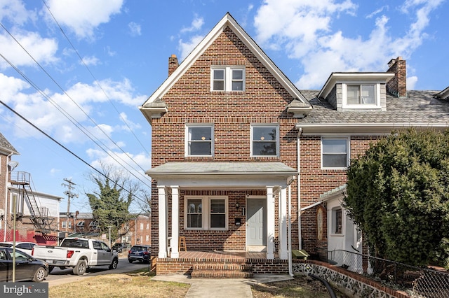 traditional home with a porch, brick siding, fence, and a shingled roof