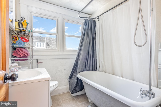 bathroom featuring toilet, tile patterned floors, a textured ceiling, vanity, and a freestanding tub