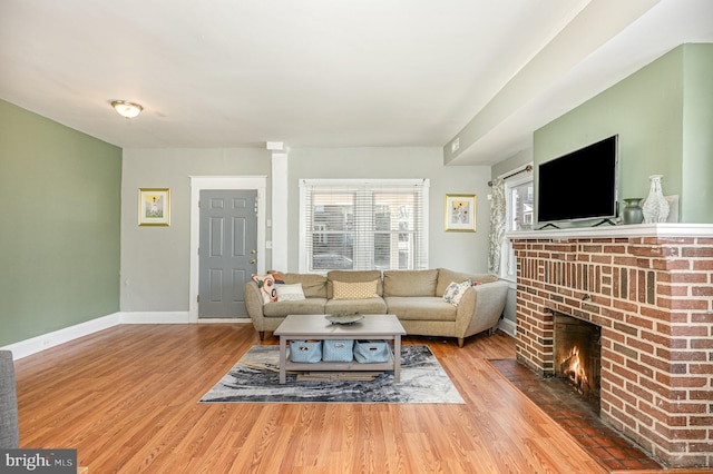 living room with a brick fireplace, baseboards, and wood finished floors