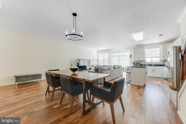 dining space with ornamental molding, sink, a notable chandelier, and light hardwood / wood-style flooring