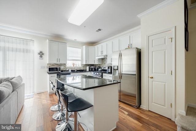 kitchen featuring a breakfast bar area, crown molding, a center island, stainless steel appliances, and white cabinets