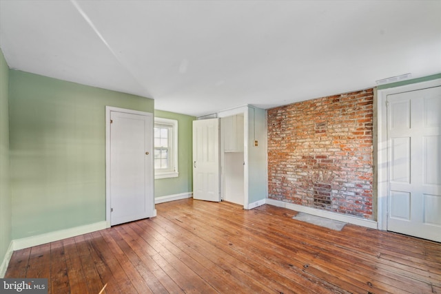 unfurnished room with hardwood / wood-style floors and brick wall