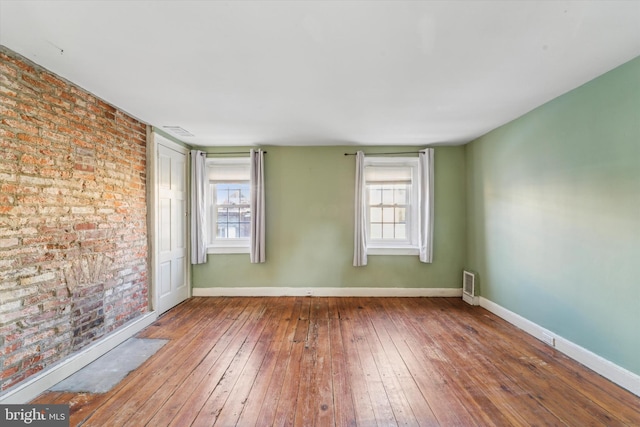 unfurnished room with brick wall, plenty of natural light, and wood-type flooring