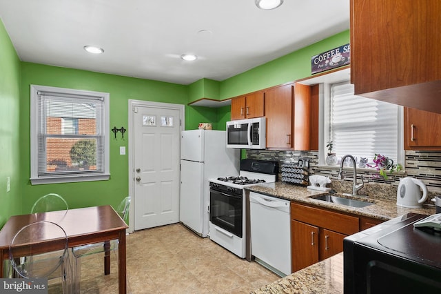 kitchen with tasteful backsplash, sink, light stone counters, and white appliances