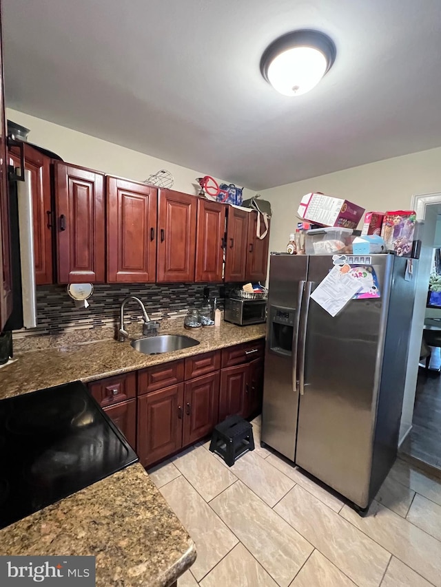 kitchen featuring stainless steel refrigerator with ice dispenser, stone countertops, black electric range, sink, and tasteful backsplash