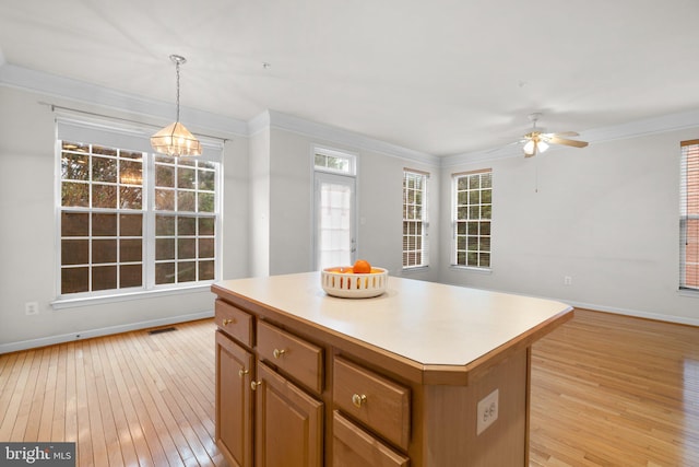 kitchen featuring a center island, decorative light fixtures, crown molding, light wood finished floors, and light countertops