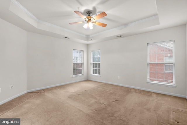 carpeted empty room featuring a tray ceiling, visible vents, ornamental molding, ceiling fan, and baseboards