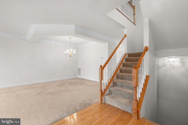 staircase featuring a notable chandelier, carpet flooring, baseboards, wood-type flooring, and crown molding