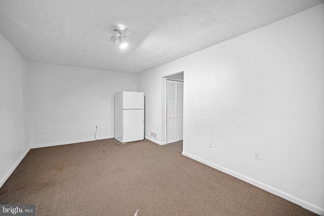 unfurnished bedroom with white refrigerator, carpet, a textured ceiling, and a closet