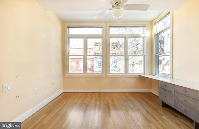 unfurnished sunroom with a ceiling fan and built in desk