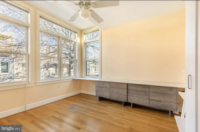 unfurnished sunroom featuring a ceiling fan and built in study area