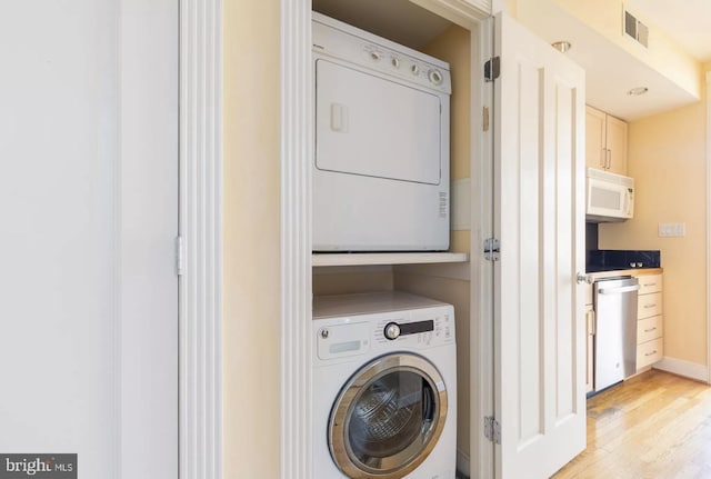 laundry area featuring laundry area, baseboards, visible vents, stacked washer / drying machine, and light wood-style floors