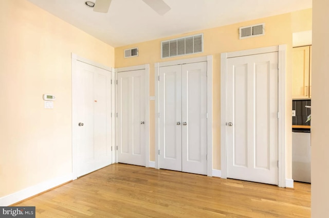 unfurnished bedroom with light wood-style floors, visible vents, and two closets