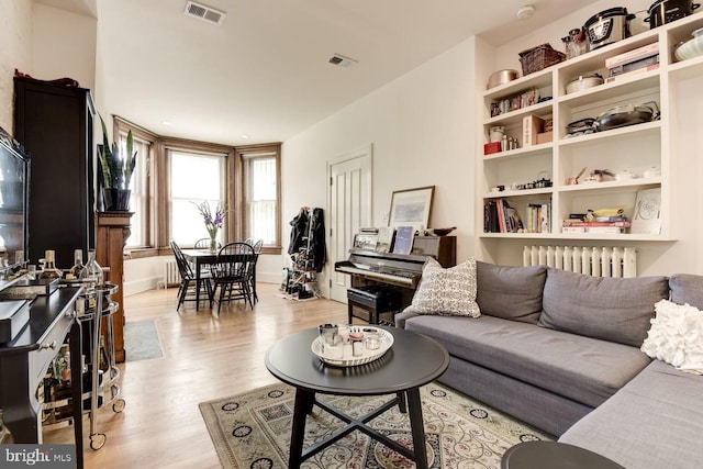 living area featuring radiator heating unit, light wood-type flooring, and visible vents