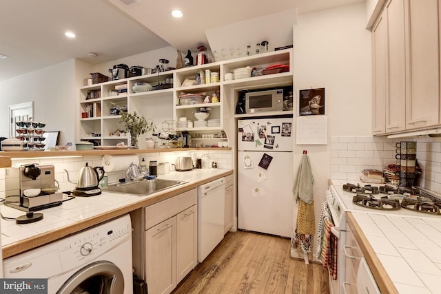 kitchen featuring tile counters, washer / clothes dryer, white appliances, and a sink