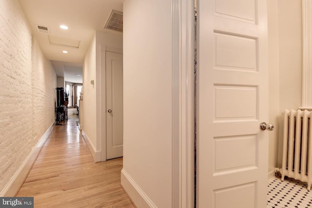 corridor featuring brick wall, radiator heating unit, visible vents, and attic access