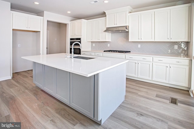 kitchen with white cabinetry, light hardwood / wood-style floors, and a center island with sink