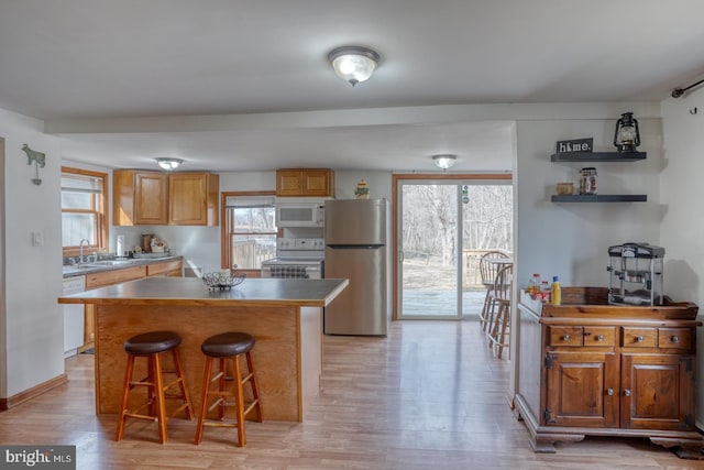 kitchen with sink, a center island, light wood-type flooring, a kitchen breakfast bar, and white appliances