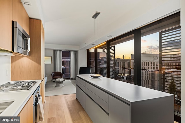 kitchen featuring a kitchen island, appliances with stainless steel finishes, sink, hanging light fixtures, and light hardwood / wood-style flooring