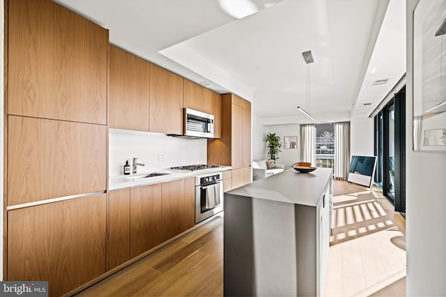 kitchen with sink, a center island, hanging light fixtures, light hardwood / wood-style flooring, and stainless steel appliances