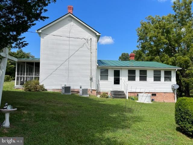 rear view of property with cooling unit, a sunroom, and a lawn