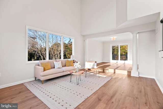 living room with a high ceiling, ornate columns, hardwood / wood-style floors, and crown molding