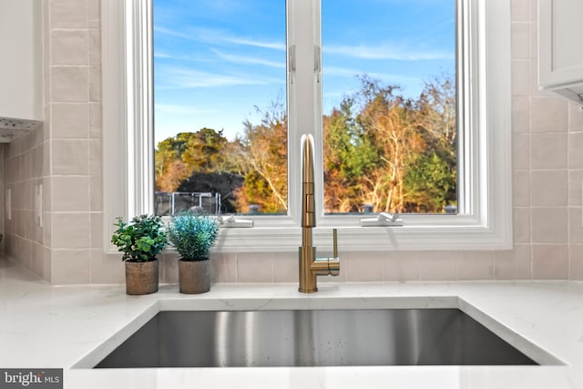 interior details featuring sink, white cabinets, and light stone counters