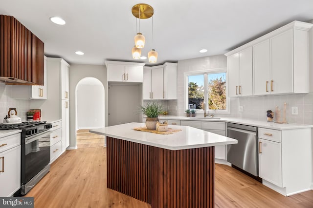 kitchen featuring white cabinets, appliances with stainless steel finishes, a center island, decorative light fixtures, and light hardwood / wood-style floors