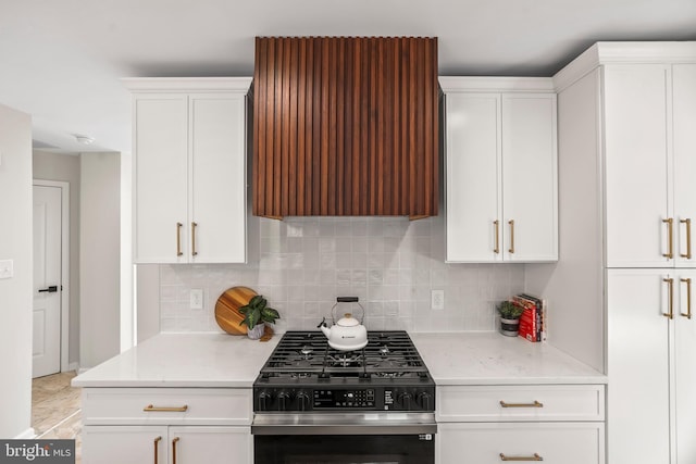 kitchen with white cabinets, range with gas stovetop, light stone countertops, and tasteful backsplash